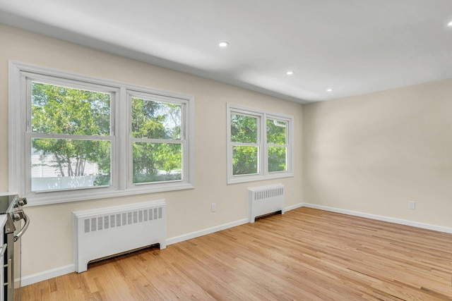 empty room featuring radiator, healthy amount of natural light, light wood-style flooring, and recessed lighting