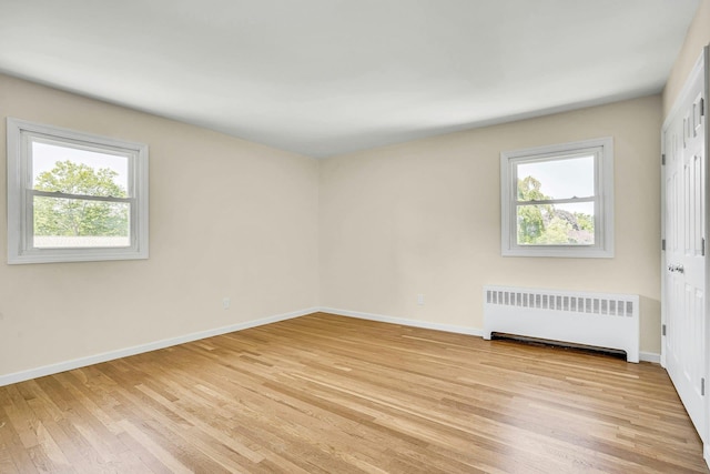 unfurnished room featuring radiator, healthy amount of natural light, light wood-style flooring, and baseboards