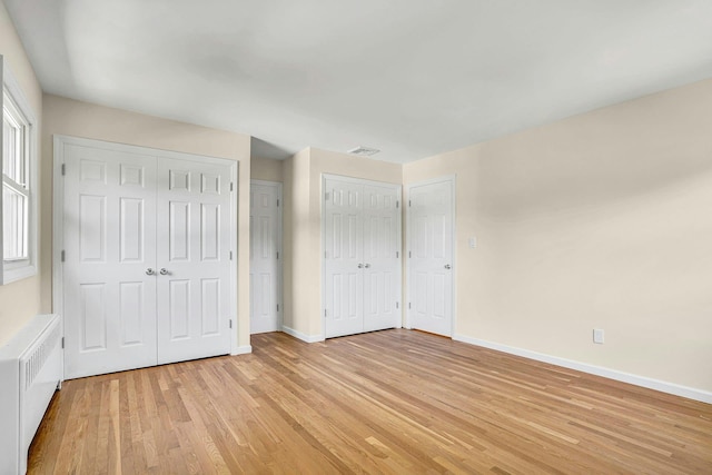 unfurnished bedroom with multiple closets, radiator heating unit, light wood-type flooring, and baseboards