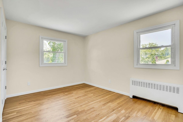 empty room with radiator, light wood finished floors, and baseboards