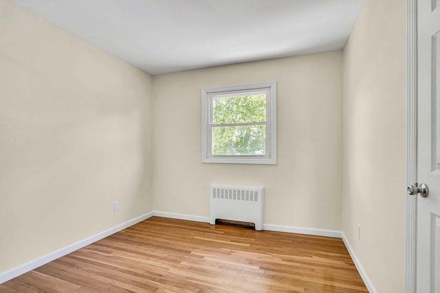 empty room with radiator, light wood-type flooring, and baseboards