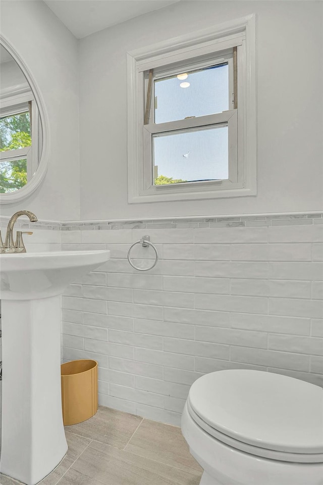 half bath featuring tile walls, toilet, and a wainscoted wall