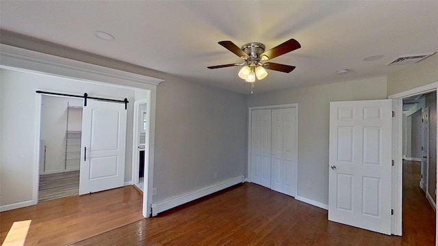 unfurnished bedroom featuring baseboard heating, a barn door, dark wood-type flooring, and baseboards