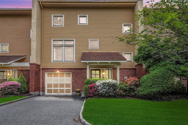 view of front facade with an attached garage, asphalt driveway, brick siding, and a yard
