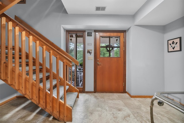 foyer entrance featuring baseboards, stone finish floors, and stairs