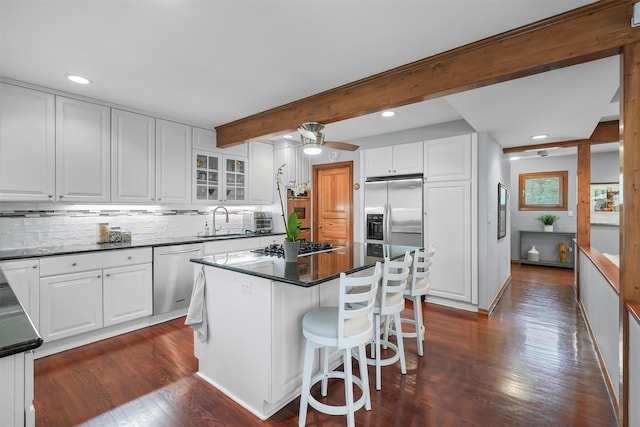 kitchen featuring appliances with stainless steel finishes, a sink, dark wood-style floors, dark countertops, and decorative backsplash