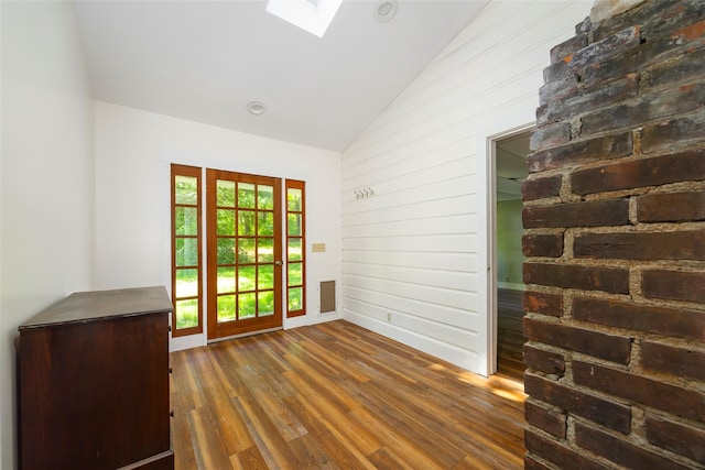 doorway featuring hardwood / wood-style flooring, baseboards, wood walls, a skylight, and high vaulted ceiling