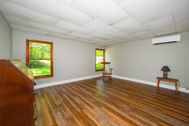 unfurnished room with a wall unit AC, wood finished floors, baseboards, and a drop ceiling