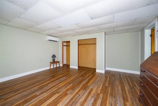 basement with a wall mounted air conditioner, dark wood-style flooring, baseboards, and a drop ceiling