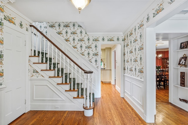74 Eakins Rd, Manhasset, NY 11030 - staircase with wallpapered walls, a wainscoted wall, wood finished floors, crown molding, and a decorative wall