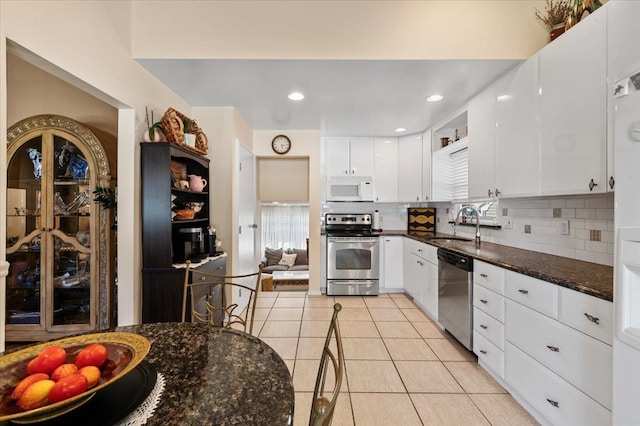 2406 Kayron Ln, North Bellmore, NY 11710 - kitchen with stainless steel appliances, light tile patterned flooring, backsplash, white cabinetry, and dark stone counters