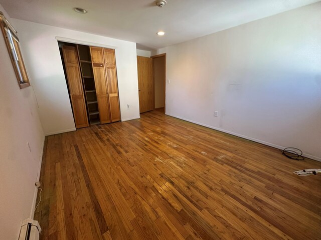 61 John St, Port Jefferson Station, NY 11776 - unfurnished bedroom featuring wood-type flooring, a baseboard radiator, recessed lighting, a closet, and baseboards