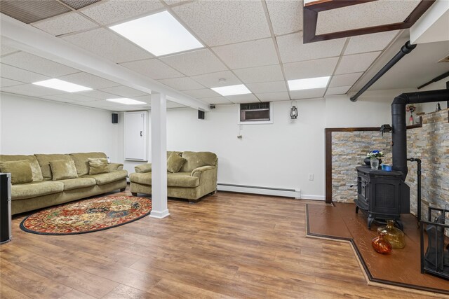 624 Westminster Rd, Baldwin, NY 11510 - living room with a baseboard heating unit, wood finished floors, a wood stove, a paneled ceiling, and baseboards