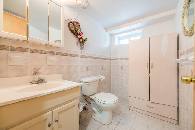 half bath featuring toilet, tile patterned floors, tile walls, vanity, and wainscoting