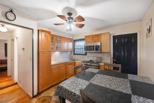 13538 129th St, South Ozone Park, NY 11420 - kitchen featuring stainless steel appliances, ceiling fan, glass insert cabinets, light wood finished floors, and a sink