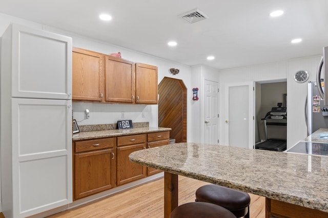 60 Heston Rd, Shirley, NY 11967 - kitchen featuring a breakfast bar area, light stone countertops, light wood finished floors, brown cabinetry, and recessed lighting
