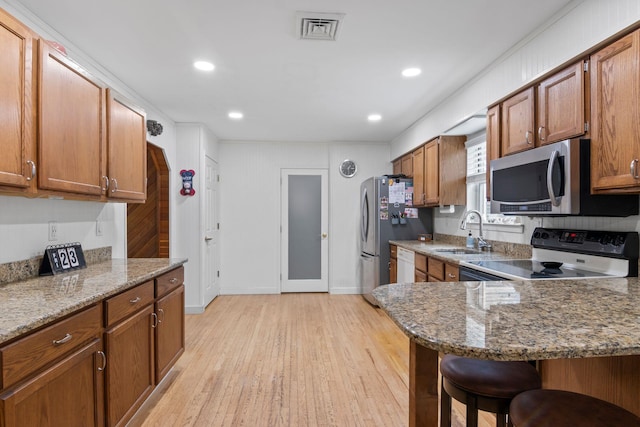 60 Heston Rd, Shirley, NY 11967 - kitchen featuring appliances with stainless steel finishes, a sink, a breakfast bar, brown cabinets, and light wood-type flooring