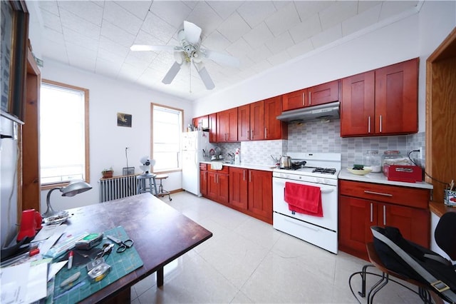 kitchen featuring white appliances, reddish brown cabinets, under cabinet range hood, tasteful backsplash, and light countertops