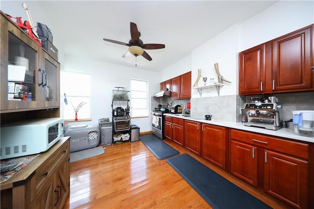 kitchen featuring white microwave, under cabinet range hood, stainless steel stove, light wood-style floors, and ceiling fan