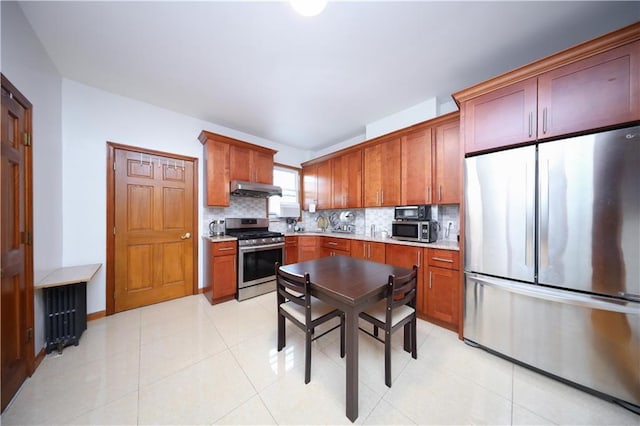 kitchen with appliances with stainless steel finishes, under cabinet range hood, decorative backsplash, light countertops, and brown cabinetry