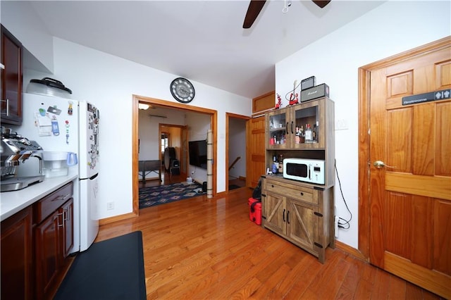 kitchen featuring white appliances, a ceiling fan, light wood-style floors, light countertops, and baseboards