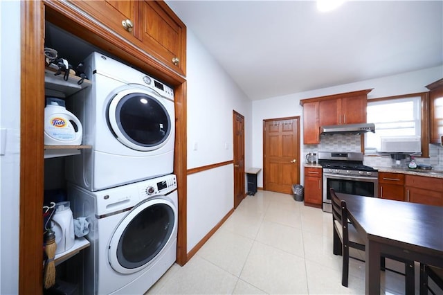 laundry area with stacked washing machine and dryer, baseboards, and light tile patterned floors