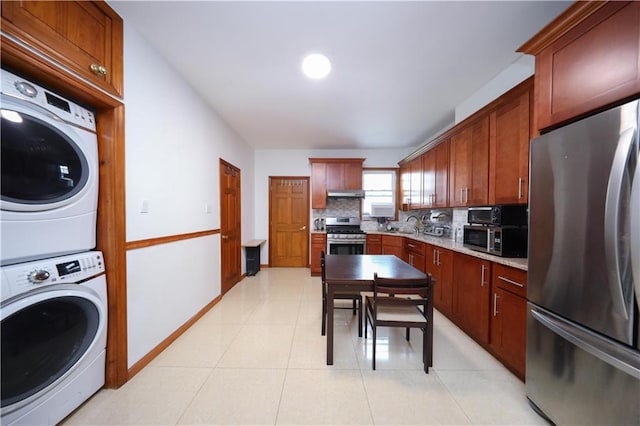 kitchen with appliances with stainless steel finishes, stacked washing machine and dryer, tasteful backsplash, under cabinet range hood, and light tile patterned floors