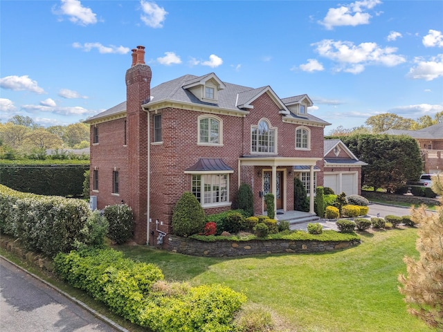 colonial house with brick siding, a chimney, a front yard, and a garage