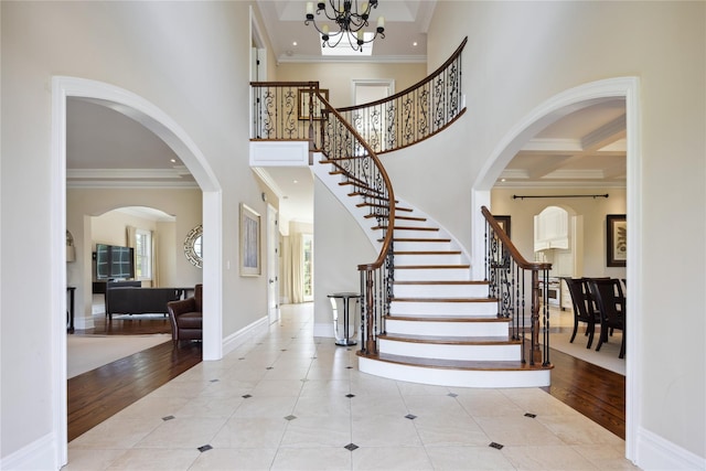 tiled foyer entrance with a high ceiling, stairs, crown molding, plenty of natural light, and a chandelier