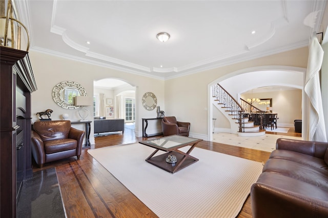 living area with arched walkways, dark wood-style floors, stairs, crown molding, and a chandelier