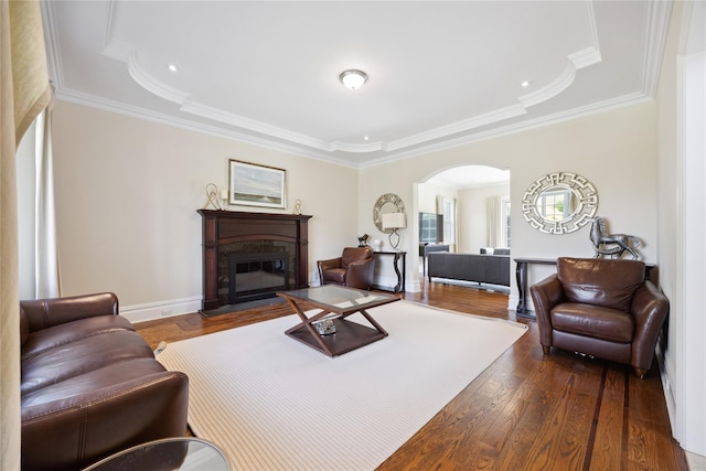 living area featuring arched walkways, a raised ceiling, dark wood-style floors, a premium fireplace, and ornamental molding