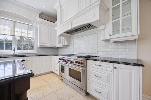 kitchen with range with two ovens, a sink, light tile patterned floors, white cabinets, and glass insert cabinets