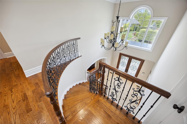 stairway with a chandelier, wood finished floors, a high ceiling, baseboards, and arched walkways