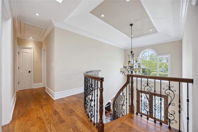 hallway with attic access, an upstairs landing, a raised ceiling, a chandelier, and wood finished floors