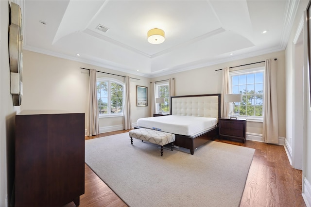 bedroom featuring a tray ceiling, wood finished floors, baseboards, and ornamental molding