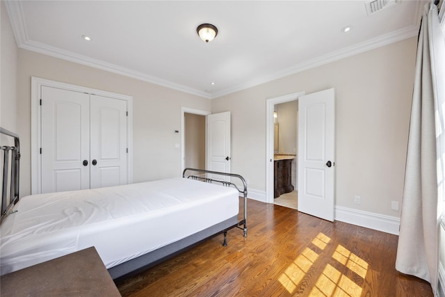 bedroom featuring baseboards, a closet, wood finished floors, crown molding, and connected bathroom