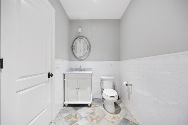 half bath with toilet, a wainscoted wall, vanity, and tile walls