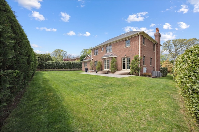 rear view of house featuring a chimney, a patio, brick siding, central AC unit, and a lawn