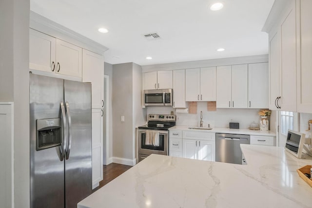 kitchen with stainless steel appliances, a sink, light stone counters, white cabinetry, and recessed lighting