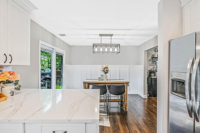 kitchen with stainless steel fridge, dark wood finished floors, white cabinets, wainscoting, and a decorative wall