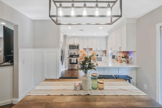 kitchen featuring appliances with stainless steel finishes, white cabinets, a peninsula, a wainscoted wall, and light countertops