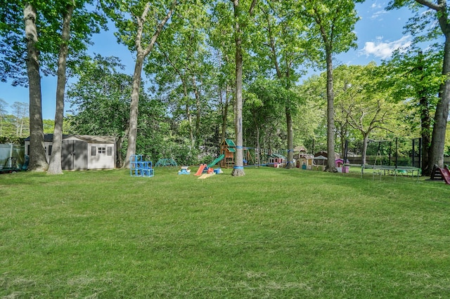view of grassy yard with a trampoline, a playground, and view of wooded area
