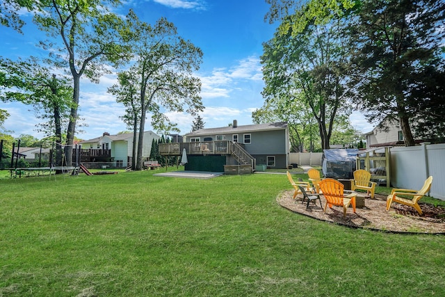 view of yard with a trampoline, a wooden deck, stairs, and an outdoor fire pit