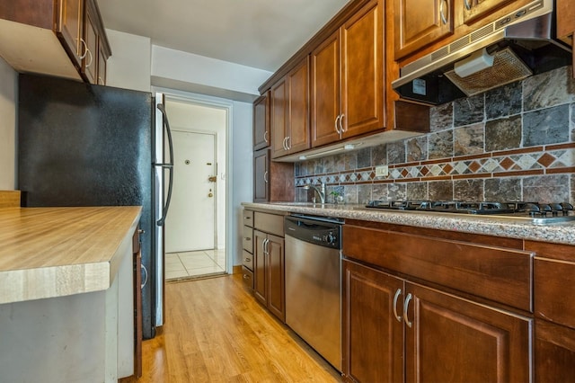 18-50 211th St Unit 2D, Bayside, NY 11360 - kitchen with under cabinet range hood, appliances with stainless steel finishes, decorative backsplash, and light wood finished floors