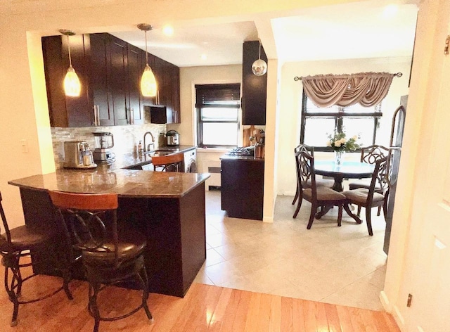 57-21 246th Cres Unit 1Fl, Douglaston, NY 11362 - kitchen with a sink, decorative backsplash, a peninsula, hanging light fixtures, and light tile patterned floors
