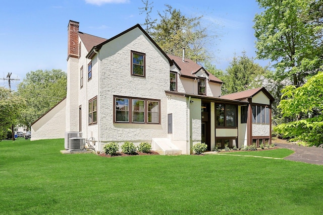 106 Garden Rd, Scarsdale, NY 10583 - view of front of house with a chimney, a sunroom, stucco siding, a front lawn, and central air condition unit