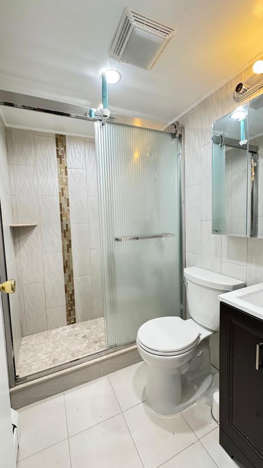 15307 79th Ave, Flushing, NY 11367 - full bathroom featuring tile patterned floors, toilet, vanity, a stall shower, and tile walls