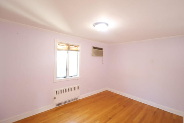 22-23 147th St, Whitestone, NY 11357 - empty room featuring radiator heating unit, light wood-style flooring, baseboards, and a wall mounted AC