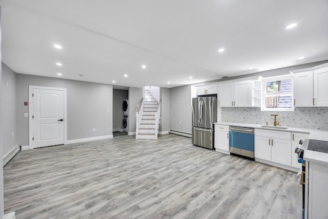 63 Ridgeway Ave, Setauket, NY 11733 - kitchen with appliances with stainless steel finishes, a baseboard radiator, stacked washing machine and dryer, a sink, and light wood-type flooring