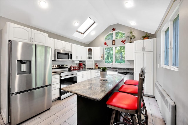 15 W Forest Ave, Freeport, NY 11520 - kitchen featuring appliances with stainless steel finishes, radiator heating unit, vaulted ceiling, backsplash, and a kitchen island